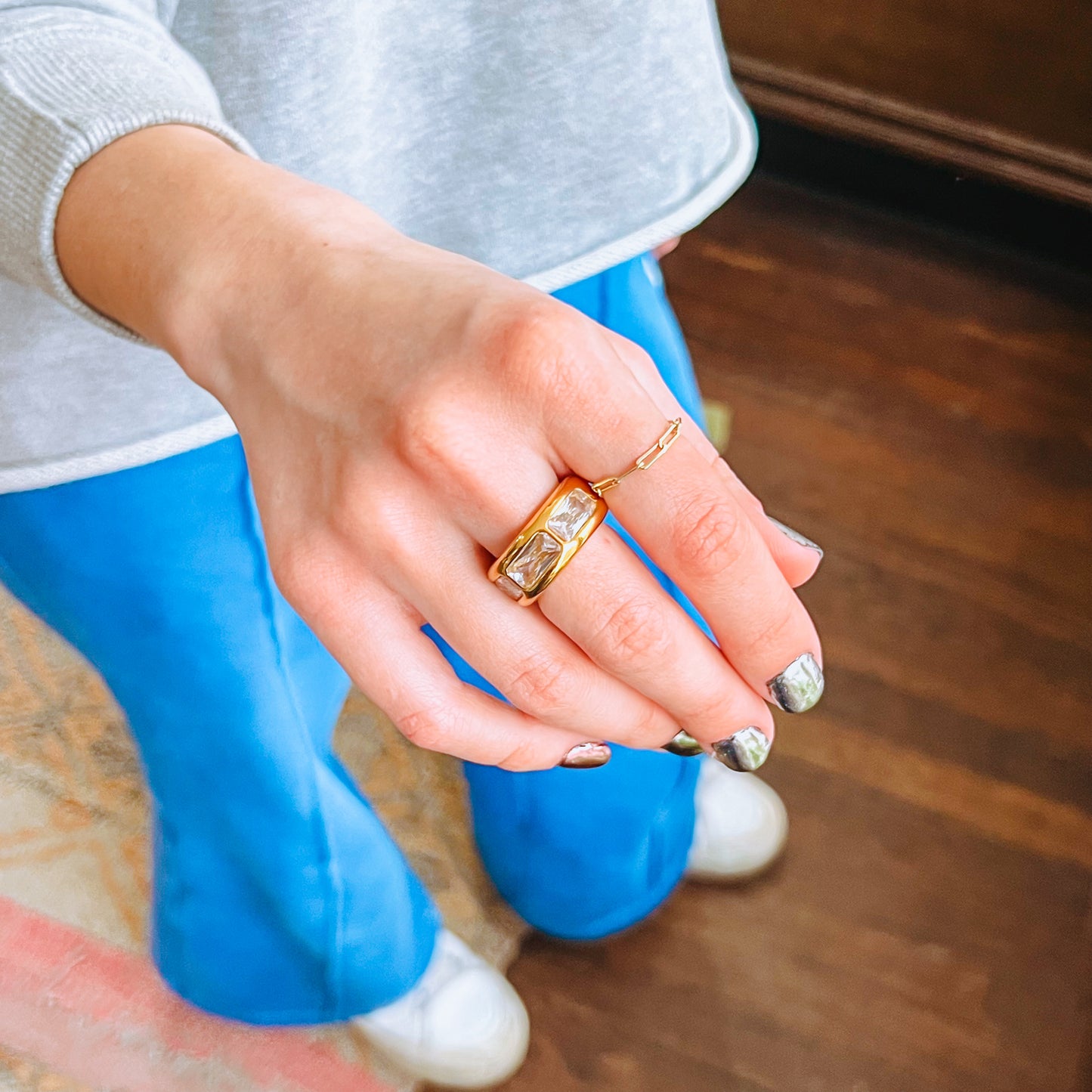 Close-up of a hand wearing a white stone vintage gold ring on a wooden floor.